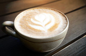 A cup of latte art coffee tulip design on wooden desk in the morning time with warm light