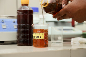 pouring used cooking oil into a measuring cup to test for FFA levels.  content of free fatty acids in used cooking oil.  the concept of dealing with household waste for renewable energy. biodiesel.