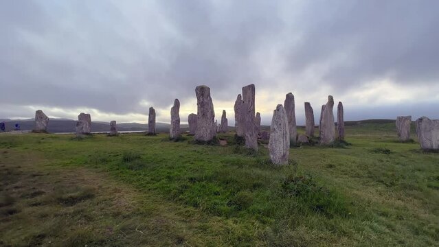 Walking towards the standing stones or megaliths of the Callanish or Calanais stone circle in a cloudy evening. Sun peeking through the could, magic, ancient, neolithic atmosphere. Archaeological site