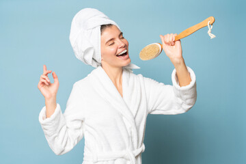Woman singing favorite song in massage brush in bathrobe with head in white towel - obrazy, fototapety, plakaty