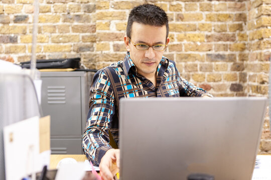 The Media Agency: Working Hard. Candid view of a creative professional concentrating on his work at his office desk. From a series of related images.