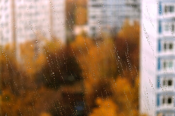 Landscape with autumn in the city view through transparent window glass with focus on rain droplets