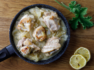 Greek stewed chicken with lemons, onions and scented leaved pelargonium leaves close-up on a iron pan on a table. horizontal, top view flat lay