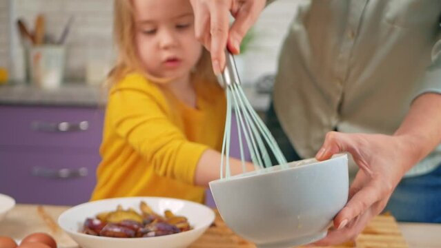 Grandmother and granddaughter cook in kitchen in middle, family pastime, leisure. woman and child make cake in purple, lavender kitchen. bowl and corolla
