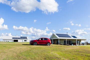 EV car on farm in country, buildings in the background have solar panels on rooves