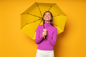 Portrait of woman in pink standing under umbrella on yellow background enjoying rainy day