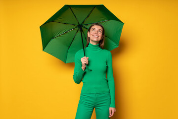 Portrait of woman standing under green umbrella on yellow background enjoying rainy day