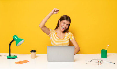 Student girl shouting with raised hand celebrating passing exam online sitting at table with laptop