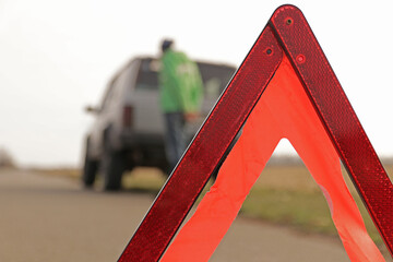 Red triangle of a stopped car on the road. An emergency stop sign mounted on the road against the background of stopped car. The concept of safe traffic on the road.