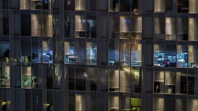 Night aerial view of office building glass panoramic window facade with illuminated lighted workspace rooms timelapse. Glowing light in skyscraper