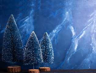 Christmas simple postcard. Decorative blue holiday trees on dark blue textured background. Scandinavian minimalistic style. Still life. Place for text.