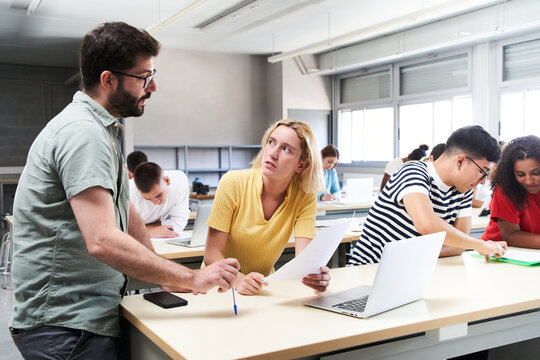 Young male teacher helping female student in class. The tutor helping his students by explaining the lesson and solving doubts. High quality photo