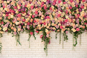 Beautiful decorative colorful roses and peonies on brick white wall. Interior wedding party decor. Wall with curly Flowers. Brick wall with beautiful flowers in room. Summer flowers on wall building.	