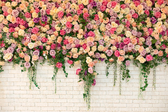 Beautiful decorative colorful roses and peonies on brick white wall. Interior wedding party decor. Wall with curly Flowers. Brick wall with beautiful flowers in room. Summer flowers on wall building.	