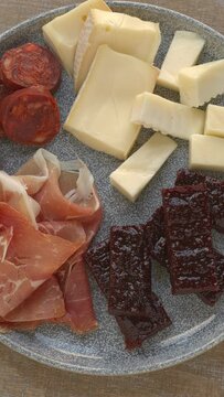 Plate with tapas: cheese, chorizo sausage, ham and membrillo sweet paste. Table spin. Vertical video.