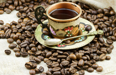 Traditional painted copper cup of coffee with heap of roasted coffee beans on sackcloth