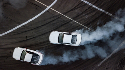 Aerial top view car drifting, Race drift car with lots of smoke from burning tires on speed track, Two car drifting battle on asphalt race track, Two drift cars battle with smoke from burned tire.