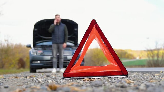 Road side warning triangle, warning oncoming traffic of a broken down car, with a man using his cell phone to call for assistance