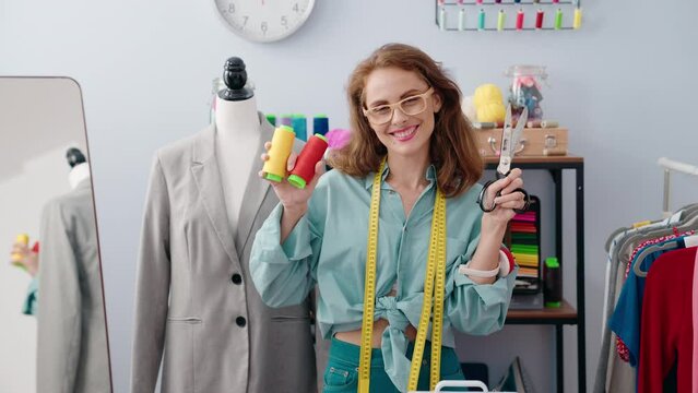 Young beautiful hispanic woman tailor smiling confident holding scissors and thread at tailor shop