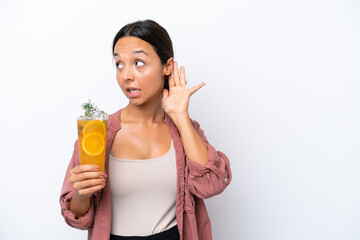 Young hispanic woman holding a cocktail isolated on white background listening to something by putting hand on the ear