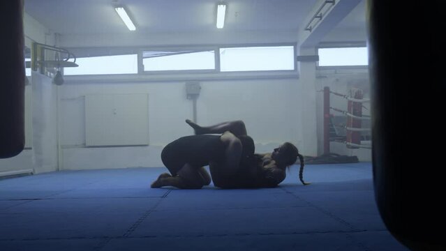 Male and female MMA fighters ground fighting workout, man and woman training punches, on floor, wide shot. Mixed martial arts practicing, long angle side view