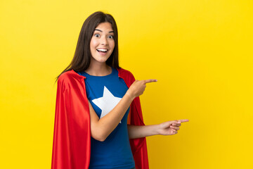 Super Hero Brazilian woman isolated on yellow background surprised and pointing side