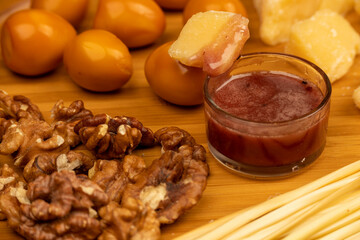 Various varieties of cheese, walnut kernels, smoked quail eggs and honey in a glass vase on a wooden surface