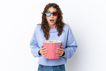 Young woman with curly hair isolated on white background surprised with 3d glasses and holding a big bucket of popcorns © luismolinero