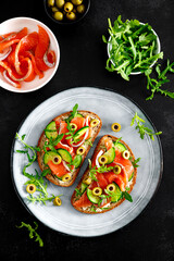 Toasts with salted salmon, arugula, green olives and cucumber. Top view