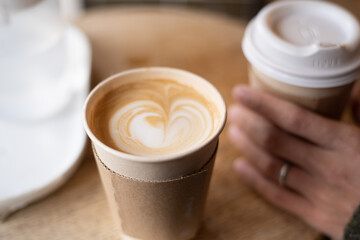 a cup of latte and a cup of coffee held by someone - obrazy, fototapety, plakaty
