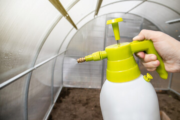 Cleaning the empty greenhouse with an antibacterial cleaner liquid, gardener hand spray it on the...