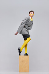 Portrait of stylish boy posing in jacket, blazer and yellow tights isolated over grey background. Weird style of youth