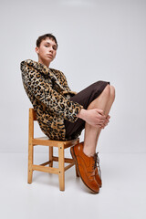 Portrait of stylish teen boy in animal print jacket and classic brogue shoes posing isolated on...