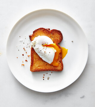 Poached egg on toasted bread on white plate with crumbs