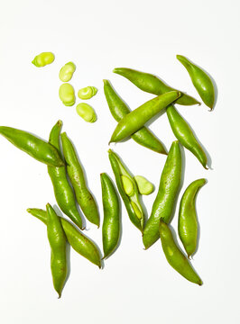 Raw fava beans on white surface in and out of shell