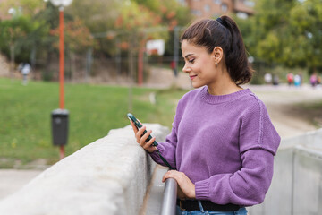 beautiful woman in purple blouse smiling outdoors looking at her mobile phone on a white bridge