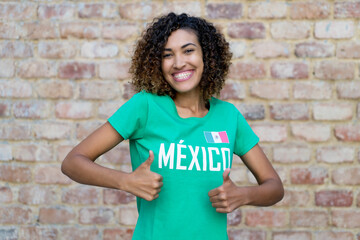 Naklejka na ściany i meble Beautiful mexican female football fan showing both thumbs up