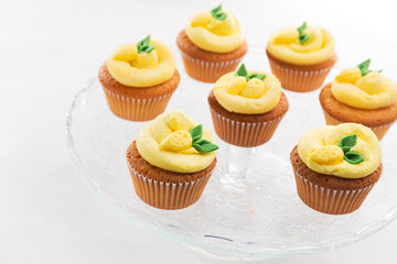 Cupcakes with lemon buttercream decorated with a lemon-shaped fondant figure with green leaves on a glass plate and white background, lactose-free product