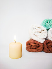 Obraz na płótnie Canvas candle is burning and next to it in the background are a pile of towels, white background, massage room, spa treatments, aroma candle,
