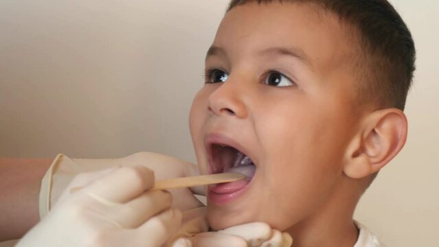 The doctor uses a spatula to examine the boy's throat.