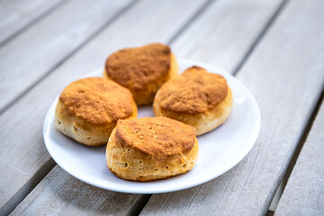 Macro closeup on four cooked homemade buttermilk breakfast biscuits on white plate at kitchen wooden table