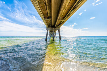Under Okaloosa island fishing pier, Fort Walton Beach, Florida panhandle with wooden pillars, waves in Gulf of Mexico with sun path water reflection