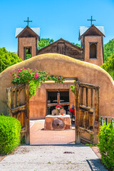 Naklejka premium Famous historic El Santuario de Chimayo sanctuary church in United States with entrance gate by flowers in summer