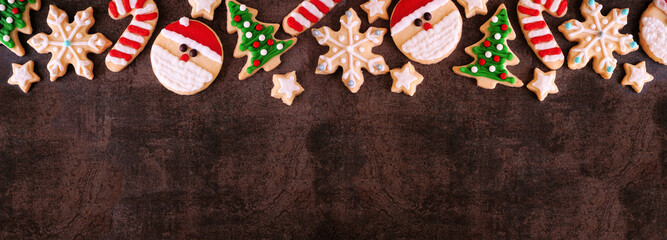 Cute Christmas cookie top border. Overhead view on a dark stone banner background with copy space....