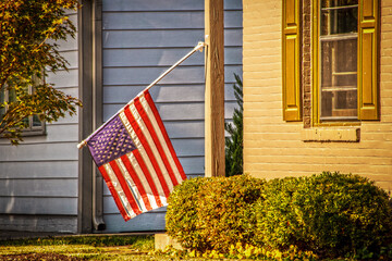 American Flag hanging downward where wind has broken its holder against house background in evening...