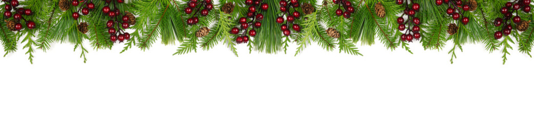Winter top border with evergreen branches, dark red berries and pine cones. Overhead view isolated on a white banner background.
