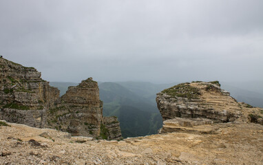 Dramatic landscape - panoramic view of the hilly valley from the Bermamyt plateau in Karachay-Cherkessia in a misty haze and stone cliffs