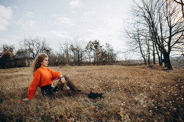 young curly girl in an orange sweater against the backdrop of autumn nature