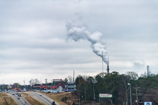 Troy, USA - January 8, 2021: Industrial smokestacks of paper mill factory plant in manufacturing Alabama city with winter cityscape by highway road