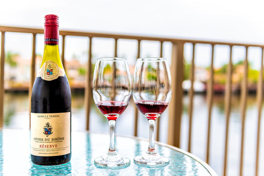 Hollywood, USA - July 12, 2021: Wineglass glasses by bottle of poured French red wine Cotes Du Rhone Famille Perrin on glass balcony in Miami, Florida